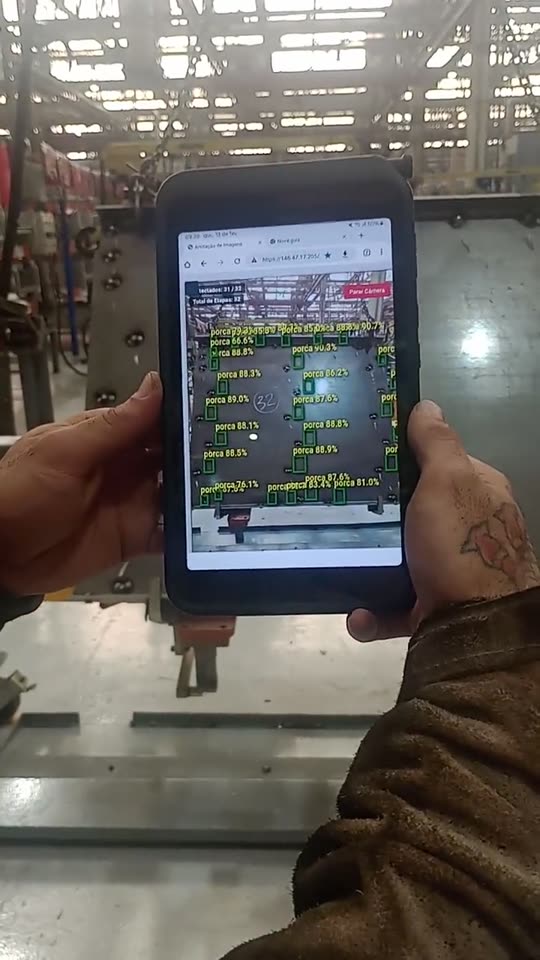 Operador segurando um tablet diante de um ferramental de grande porte, com o sistema identificando cada porca e mostrando o percentual de confiança das detecções