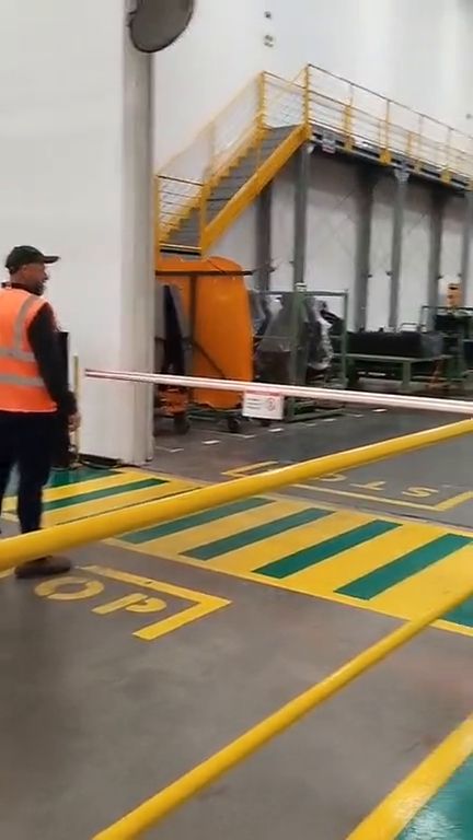 Travessia de pedestres em chão de fábrica com cancela automatizada, semáforo e faixa sinalizada no piso